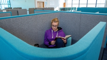 Single female student wearing a purple Hertfordshire University hoodie studying in a study booth.