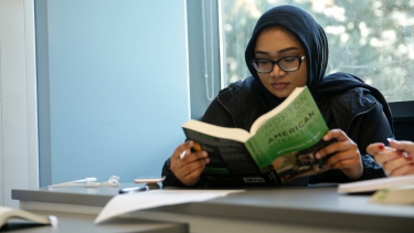 Single female student reading a book in a classroom at Hertfordshire International College