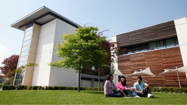 Three Hertfordshire International College students sitting out on a lawn on campus at Hertfordshire University