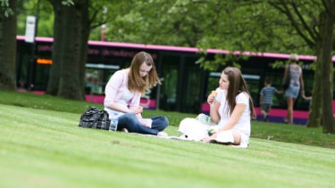 Two students of Hertfordshire International College sat on the fields at Hertfordshire University.